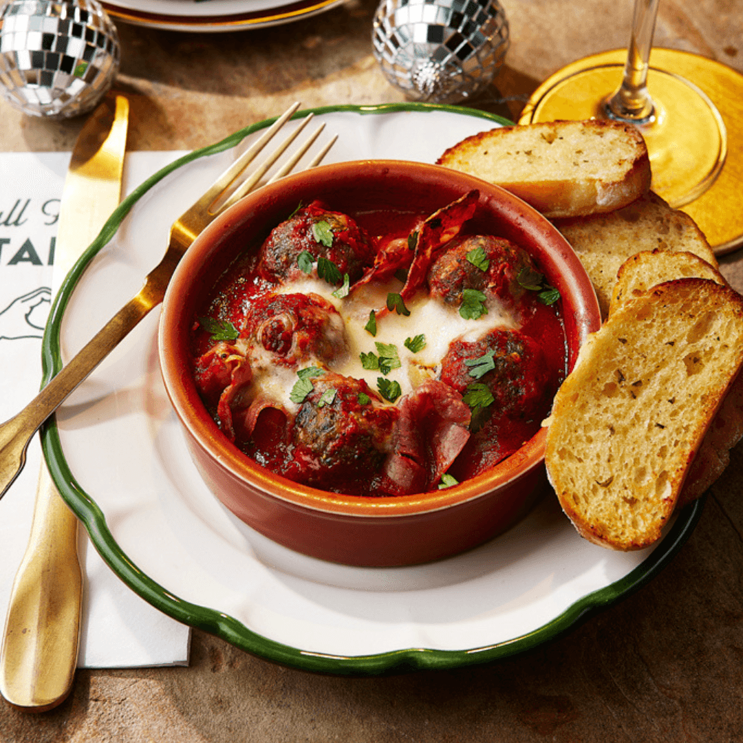 A plate of festive meatballs served at ASK Italian restaurants. The meatballs are served in a red tomato sauce with bubbling mozzarella on top.