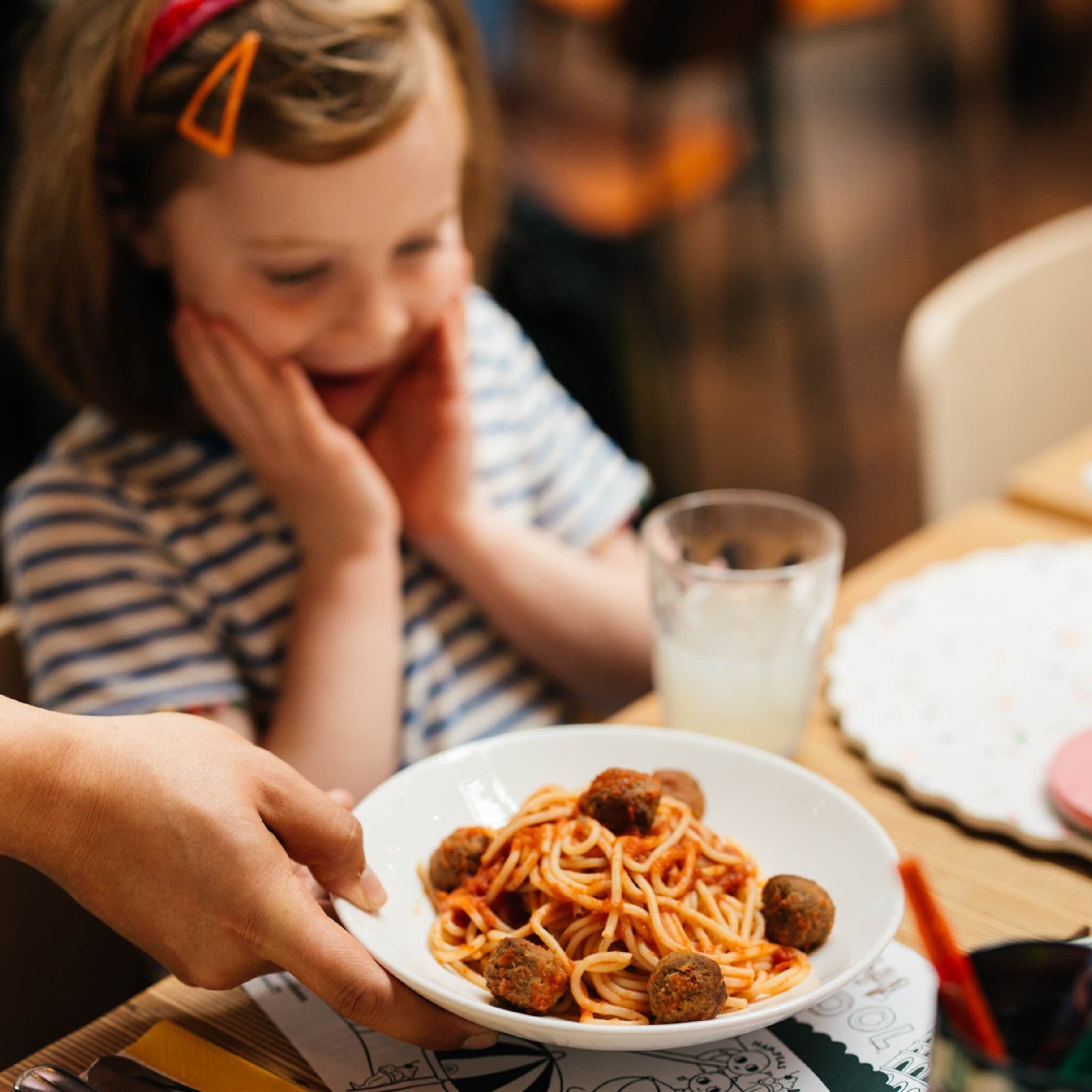 A child with a plate of pasta & meatballs