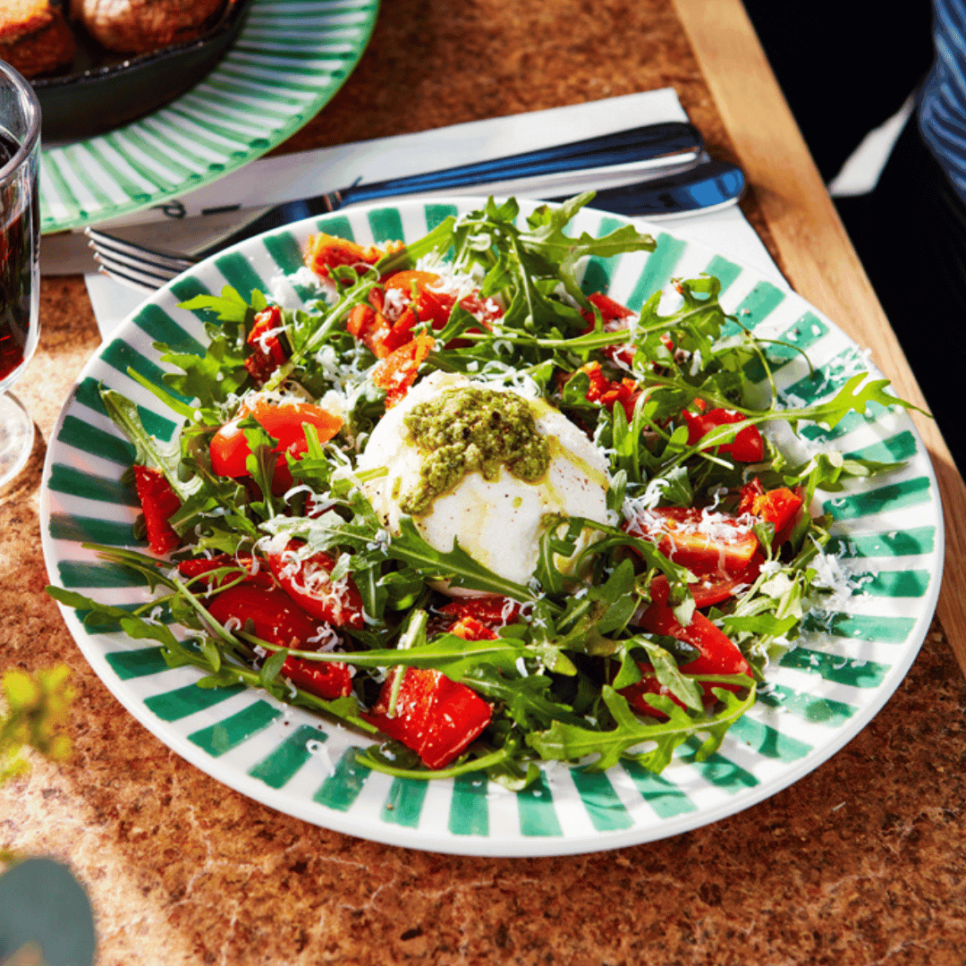 A salad featuring rocket, tomatoes and burrata with pesto.